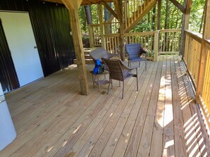 Una terraza de madera con dos sillas de mimbre y una mesa pequeña, rodeada por una barandilla de madera.