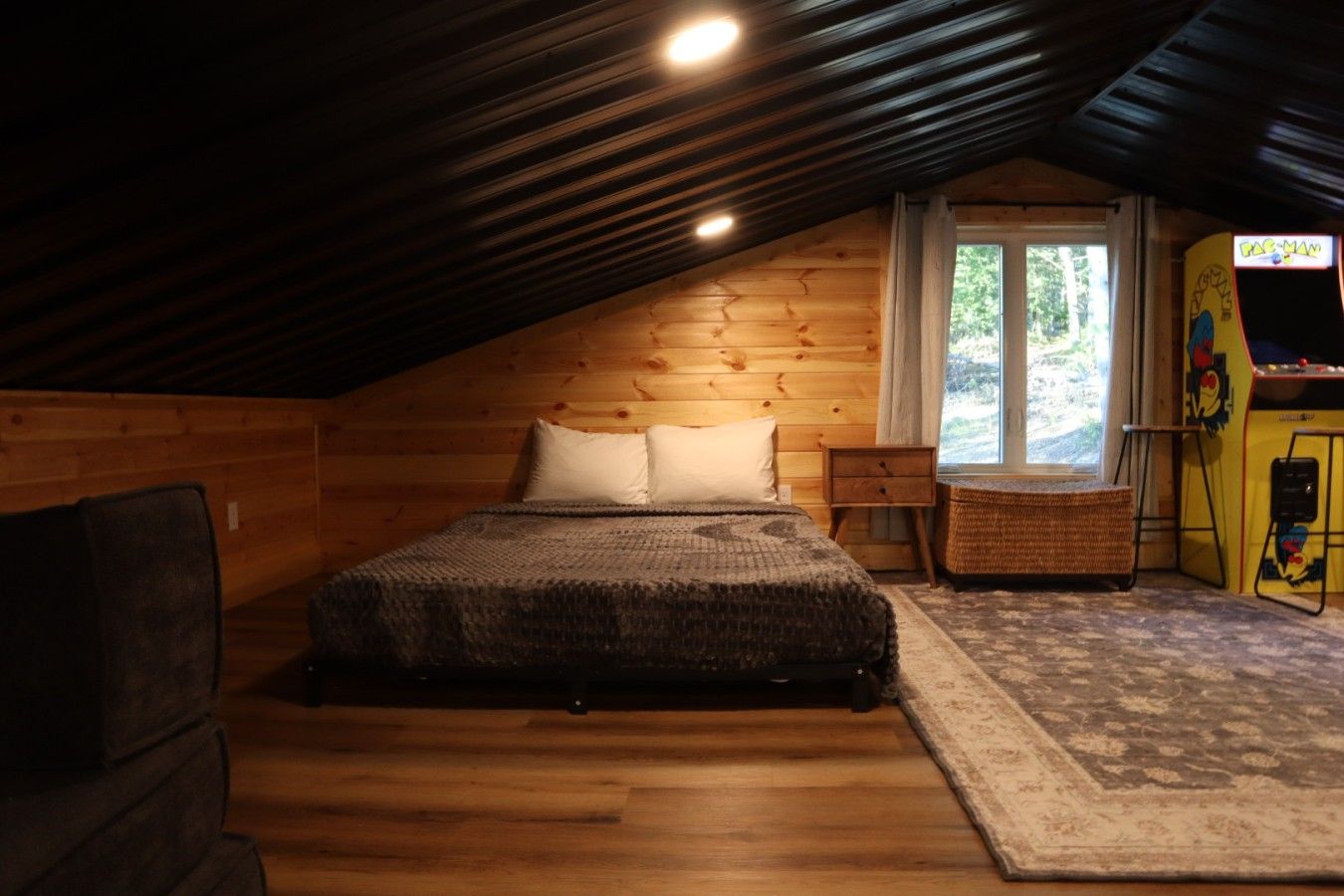 A cozy attic bedroom with a bed, a window, and a Pac-Man arcade machine.