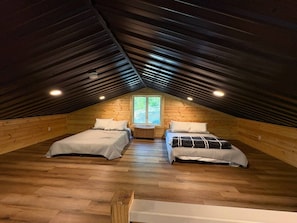 A cozy attic bedroom with two beds, wooden flooring, a window, and a sloped ceiling. - Chasin Turkeys | Lakefront Cabin w/ Hot Tub, Arcade Game & Fire Pit (Campton)