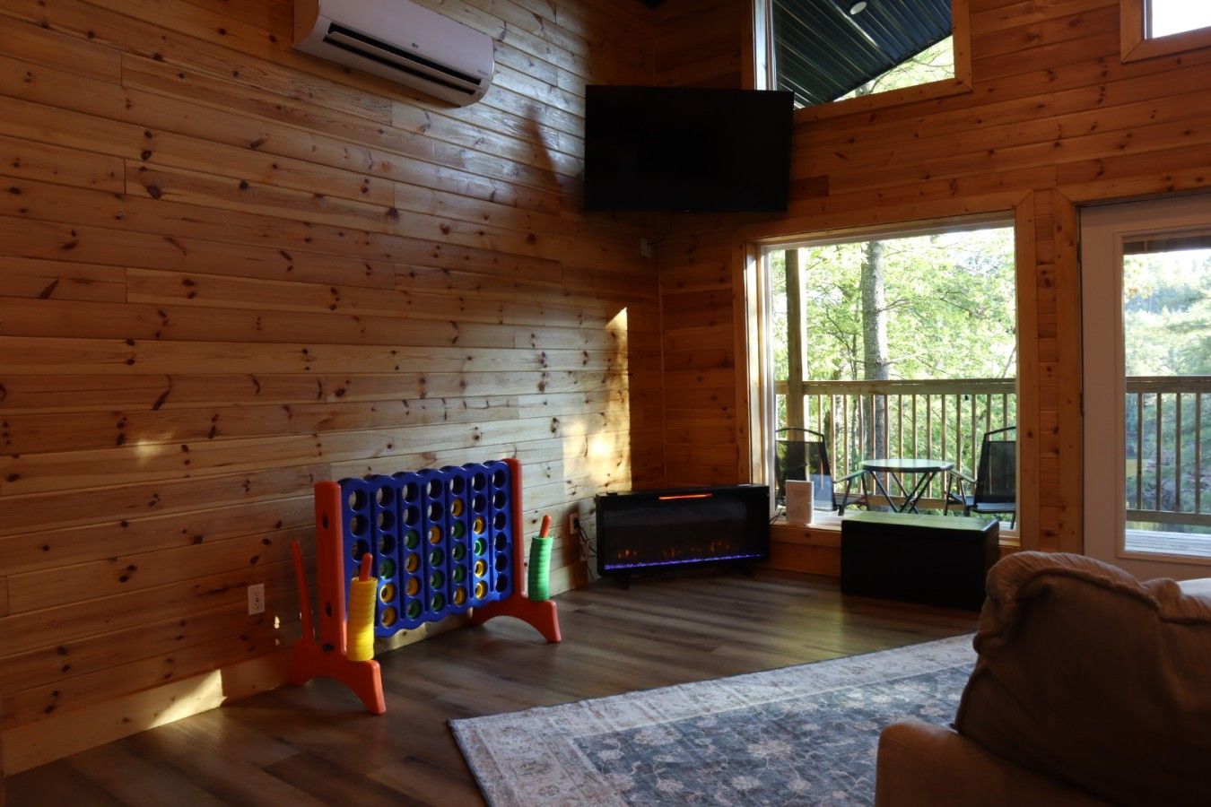 A wooden cabin interior with a television mounted on the wall, a pool table, and a large window offering a view of the outdoors.