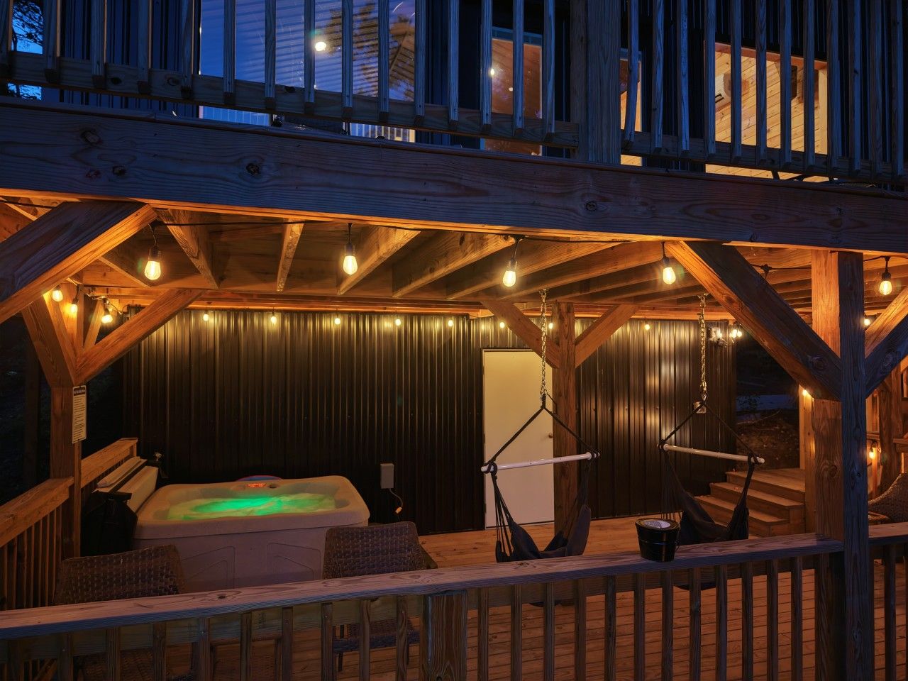 A wooden cabin with a hot tub, a hammock, and a staircase leading to a balcony.