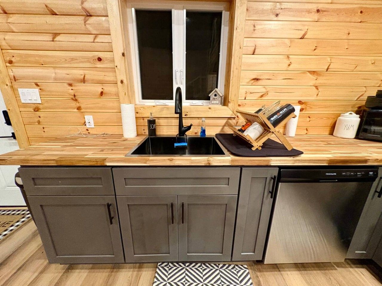 A compact kitchen with a built-in dishwasher, a double sink, and wooden cabinetry.