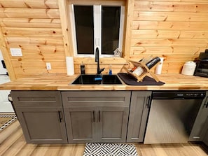 A compact kitchen with a built-in dishwasher, a double sink, and wooden cabinetry. - Chasin Turkeys | Lakefront Cabin w/ Hot Tub, Arcade Game & Fire Pit (Campton)