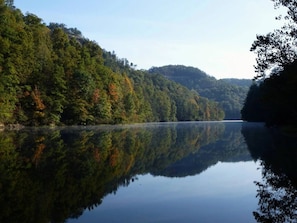 A calm lake with dense forest on both sides, reflecting the trees and sky. - Chasin Turkeys | Lakefront Cabin w/ Hot Tub, Arcade Game & Fire Pit (Campton)