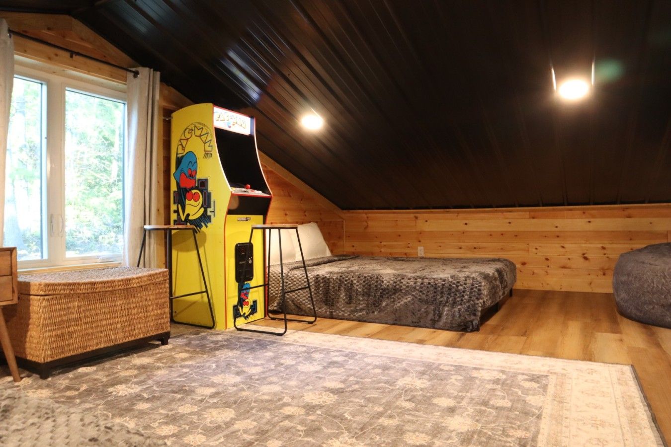 A cozy attic room with a bunk bed, a small desk, and a window with curtains.