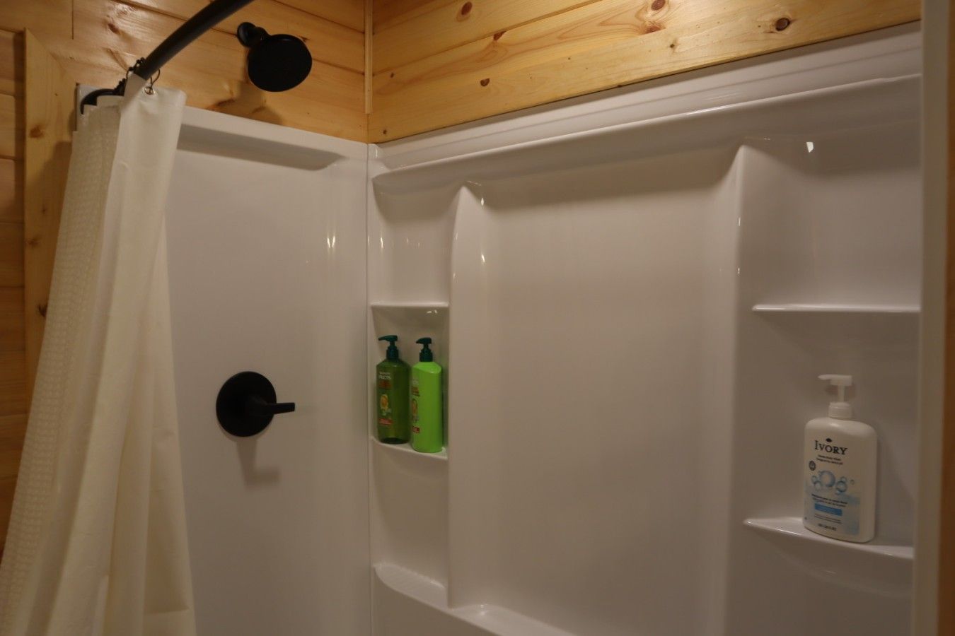 A shower area with a wooden ceiling, a white shower curtain, and a shelf with toiletries.