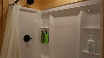 A shower area with a wooden ceiling, a white shower curtain, and a shelf with toiletries.