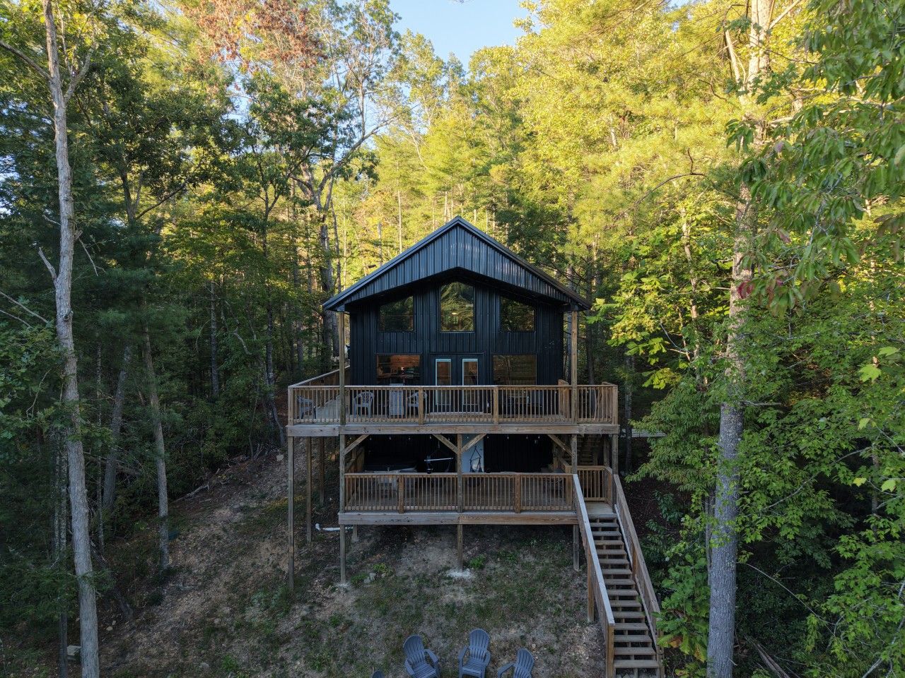 A two-story wooden cabin with a balcony, surrounded by dense forest.