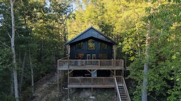 A two-story wooden cabin with a balcony, surrounded by dense forest.