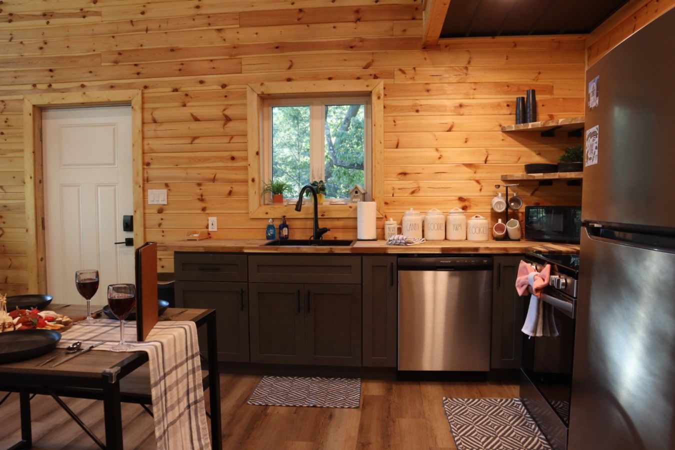 A wooden cabin kitchen with a sink, stove, refrigerator, and a dining table with chairs.