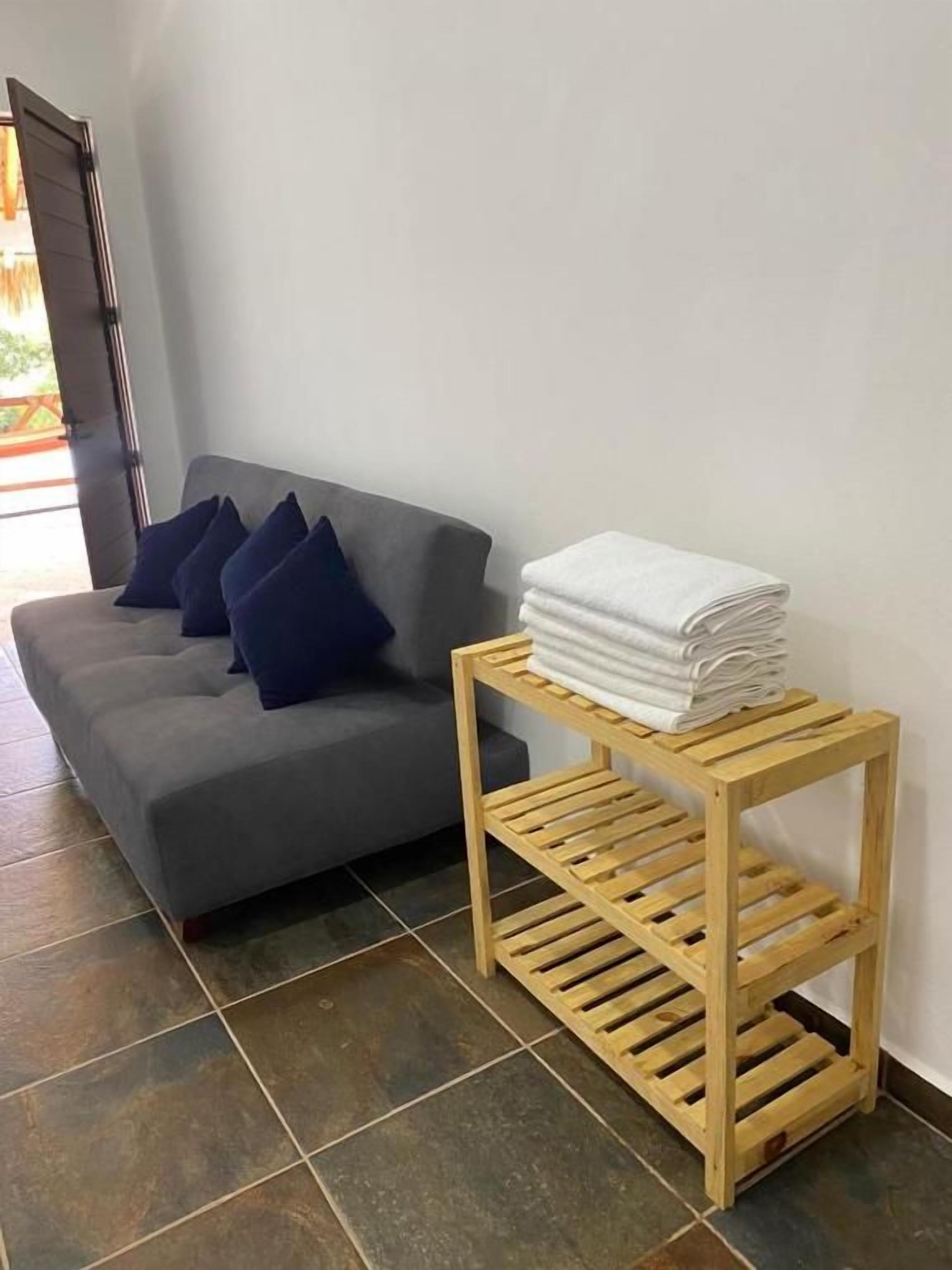 A grey sofa with blue cushions and a wooden shelf with folded towels.