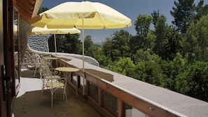 An outdoor patio with a table and chairs, a yellow umbrella, and a view of trees. - Celestial inn (Pucon)