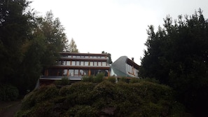 A modern two-story building with a flat roof and large windows, surrounded by dense greenery. - Celestial inn (Pucon)