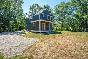A two-story house with a covered porch, surrounded by a gravel driveway and a grassy lawn. - The Blue Jetty Coastal Home (Kennebunkport)