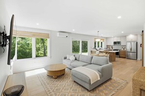 A modern living space with a sofa, round coffee table, and a kitchen area with a refrigerator and microwave. - The Blue Jetty Coastal Home (Kennebunkport)