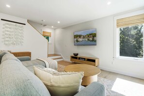 A modern living room with a sofa, coffee table, and a TV mounted on the wall. - The Blue Jetty Coastal Home (Kennebunkport)