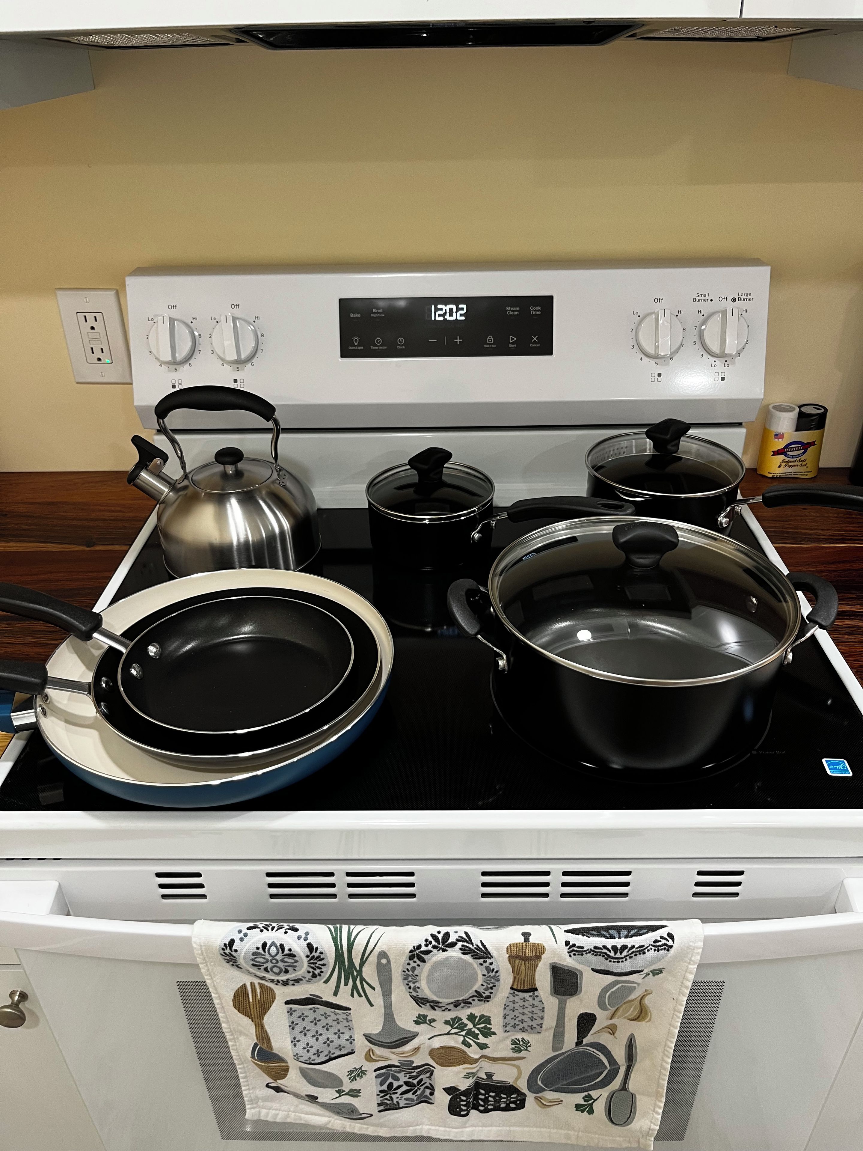 A kitchen with a stove, pots, pans, and a kettle.