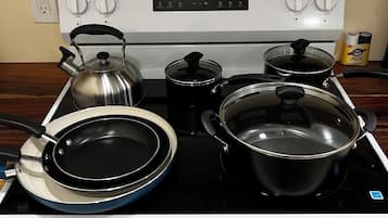 A kitchen with a stove, pots, pans, and a kettle.