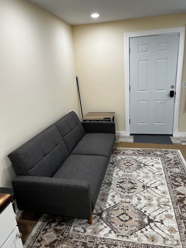 A gray sectional sofa, a patterned rug, a door, and a small table with a remote control.
