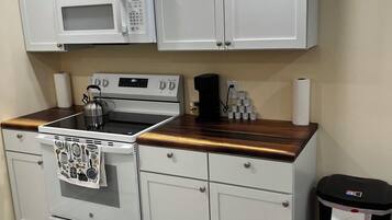Eine kompakte Küche mit weißen Schränken, einer Mikrowelle, einem Backofen und einer Kaffeemaschine.