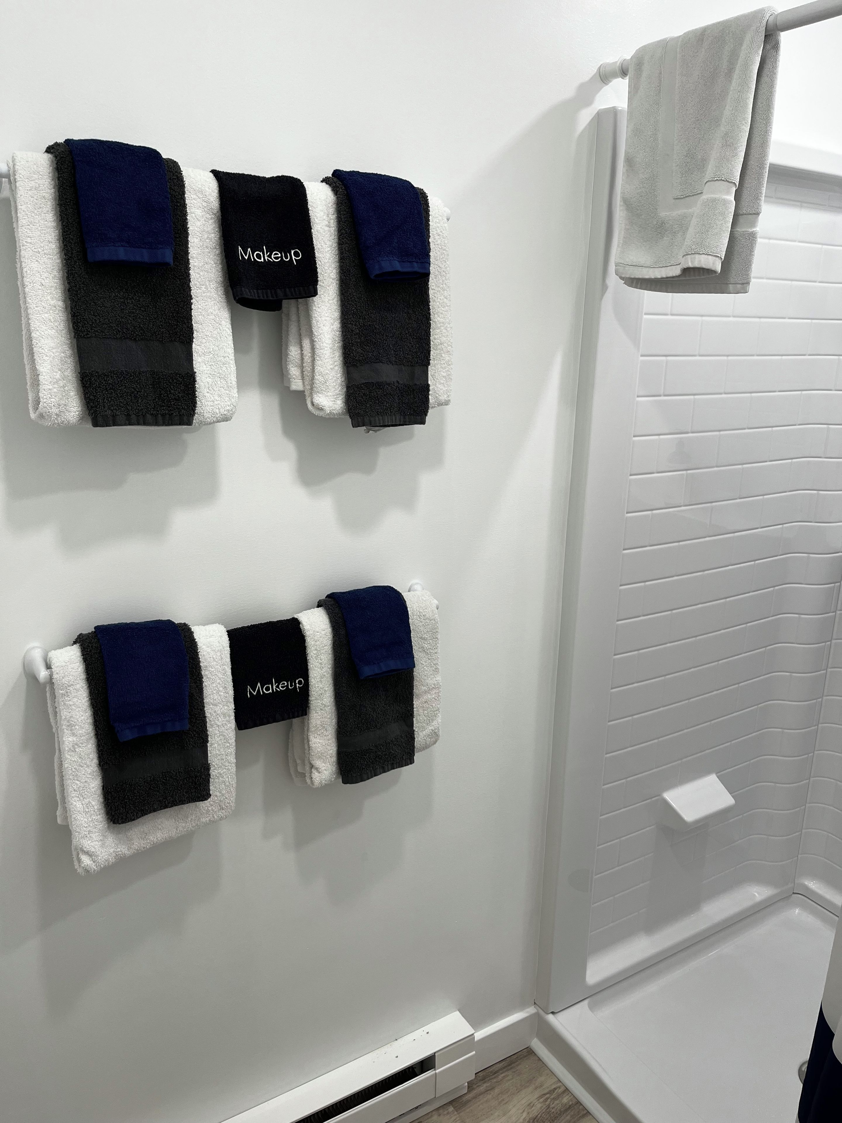 A bathroom with white tiled walls, a white towel rack with four towels, and a white shower curtain.