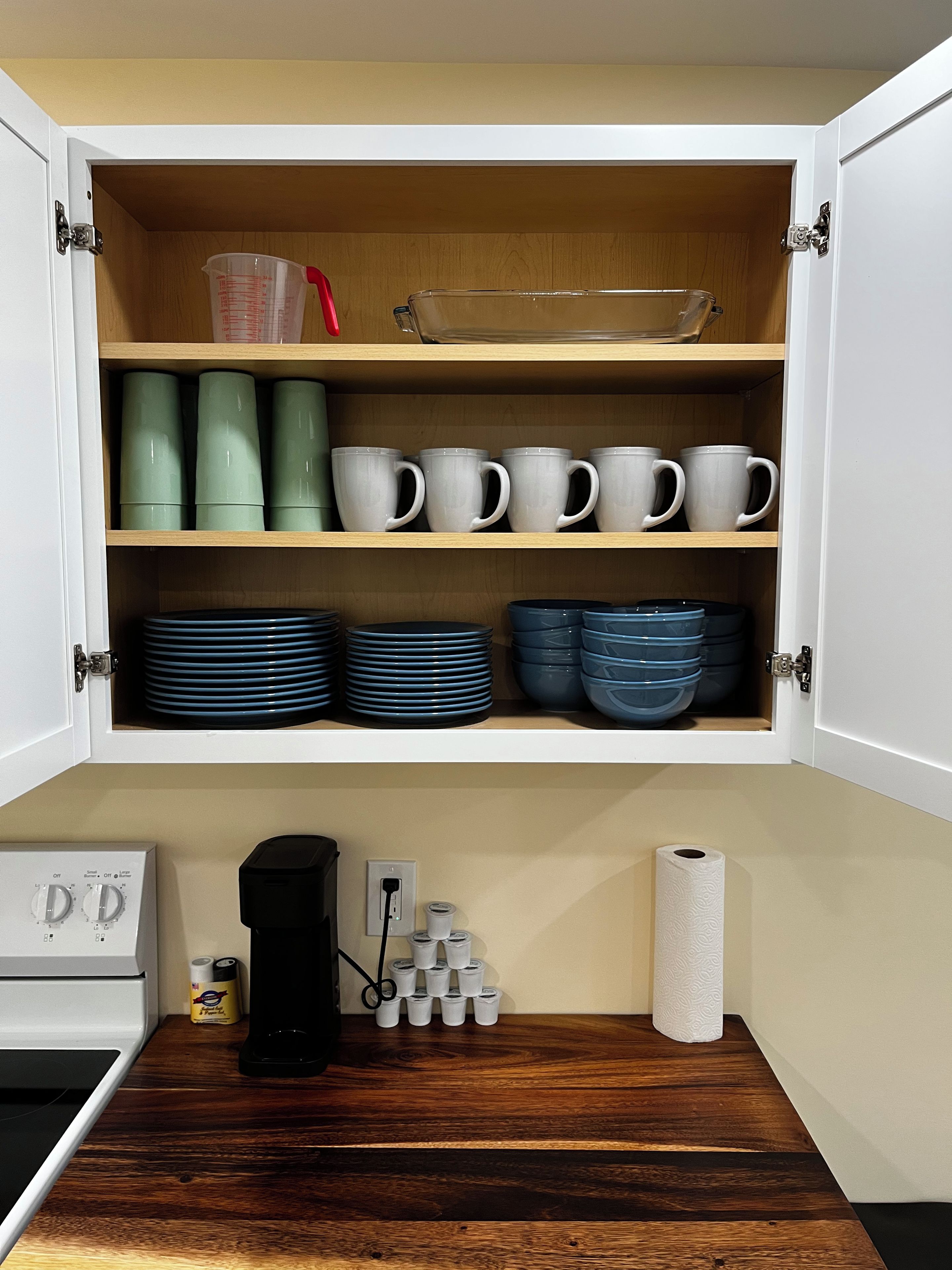A kitchen cabinet with mugs, plates, and a coffee maker.
