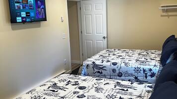 Un dormitorio con dos camas, ventilador de techo, televisor montado que muestra servicios de transmisión, y una puerta que da a otra habitación.