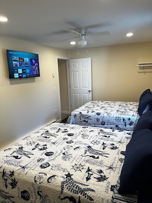 A bedroom with two beds, a ceiling fan, a mounted TV displaying streaming services, and a door leading to another room.