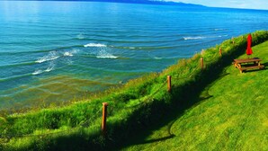 A coastal landscape with a grassy path, a wooden bench, and a red umbrella. - Beachside Studio with Property Hot Tub on Water (Homer)