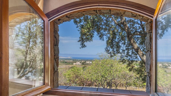 A room with a large arched window overlooking a landscape with trees and a distant view of the sea. - Maison Camellu – Propriété de charme au cœur des oliviers, vue mer (Calenzana)