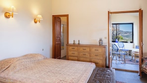 A bedroom with a bed, a dresser, a mirror, and a view of a balcony. - Maison Camellu – Propriété de charme au cœur des oliviers, vue mer (Calenzana)