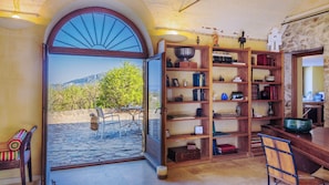 Ein Zimmer mit einem großen Bogenfenster, einem hölzernen Bücherregal und Blick auf eine gebirgige Landschaft.