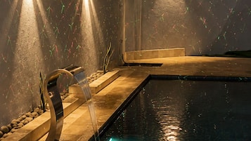 Ein Schwimmbeckenbereich mit Wasserspiel und Wandleuchten.