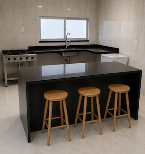 Una cocina moderna con una isla central, taburetes de bar, una estufa y un ventanal sobre el lavadero.