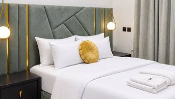A neatly made bed with white bedding and a single yellow accent pillow, a bedside table with a drawer, and a framed picture on the wall.