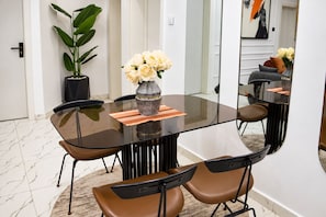 A modern dining area with a glass table, brown chairs, a vase with flowers, and a potted plant. - Nigus House Akinloye (Lekki)