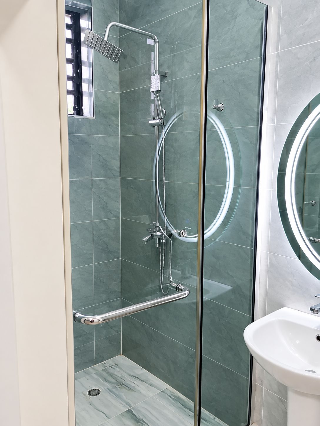 Een moderne badkamer met een douchecabine van glas, een handgreep en een wastafel met spiegel.