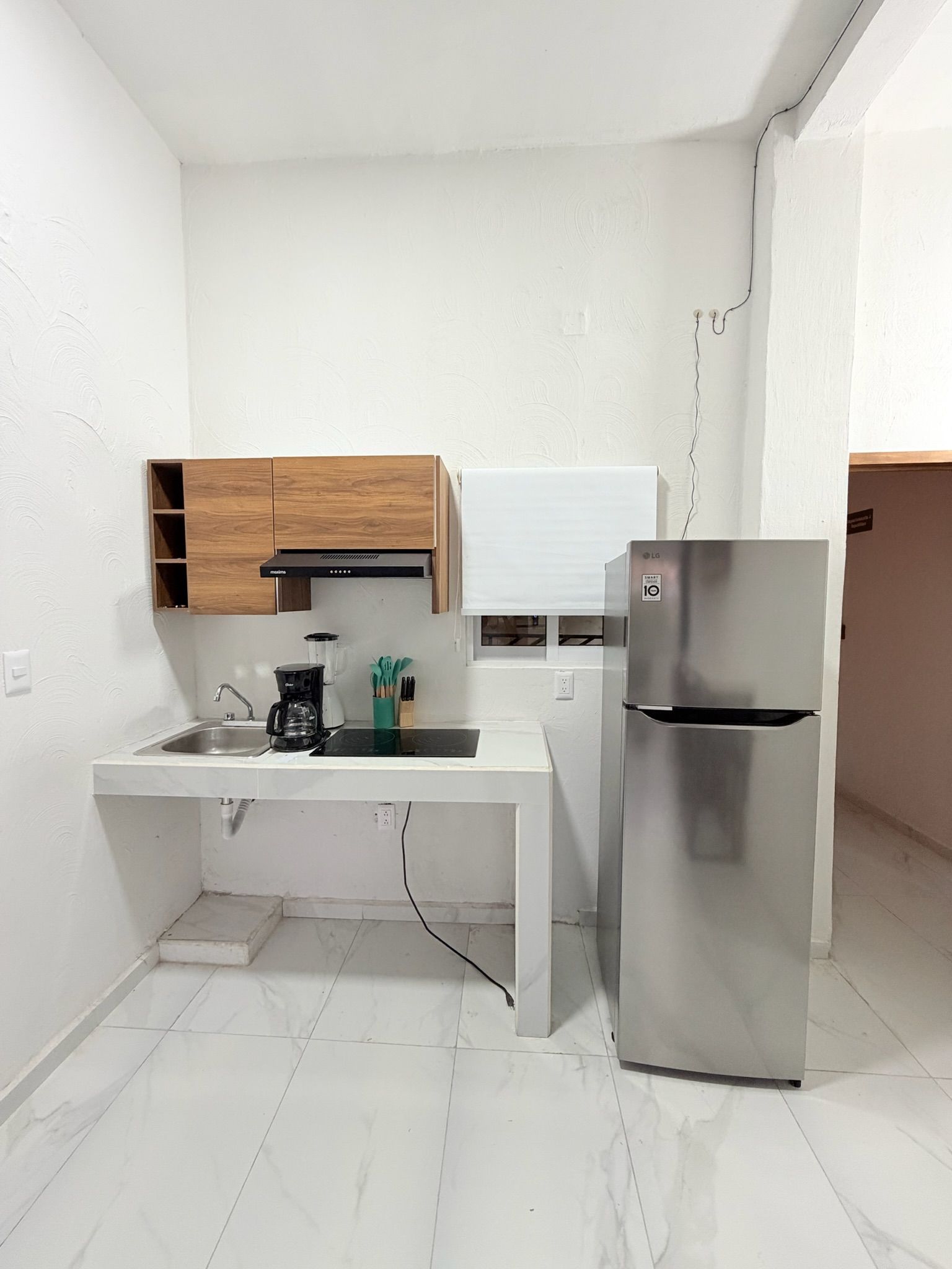 Cocina compacta con microondas integrado, refrigerador de acero inoxidable, mueble de madera y encimera blanca.