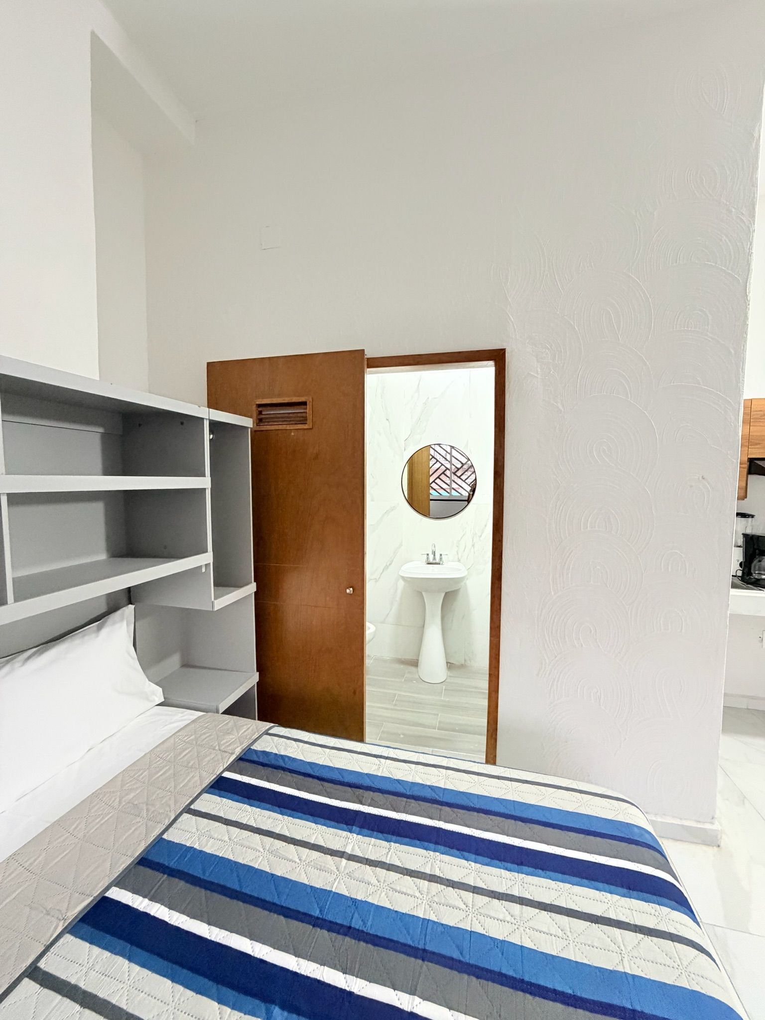 Una habitación de hotel con cama, armario, espejo y lavamanos.