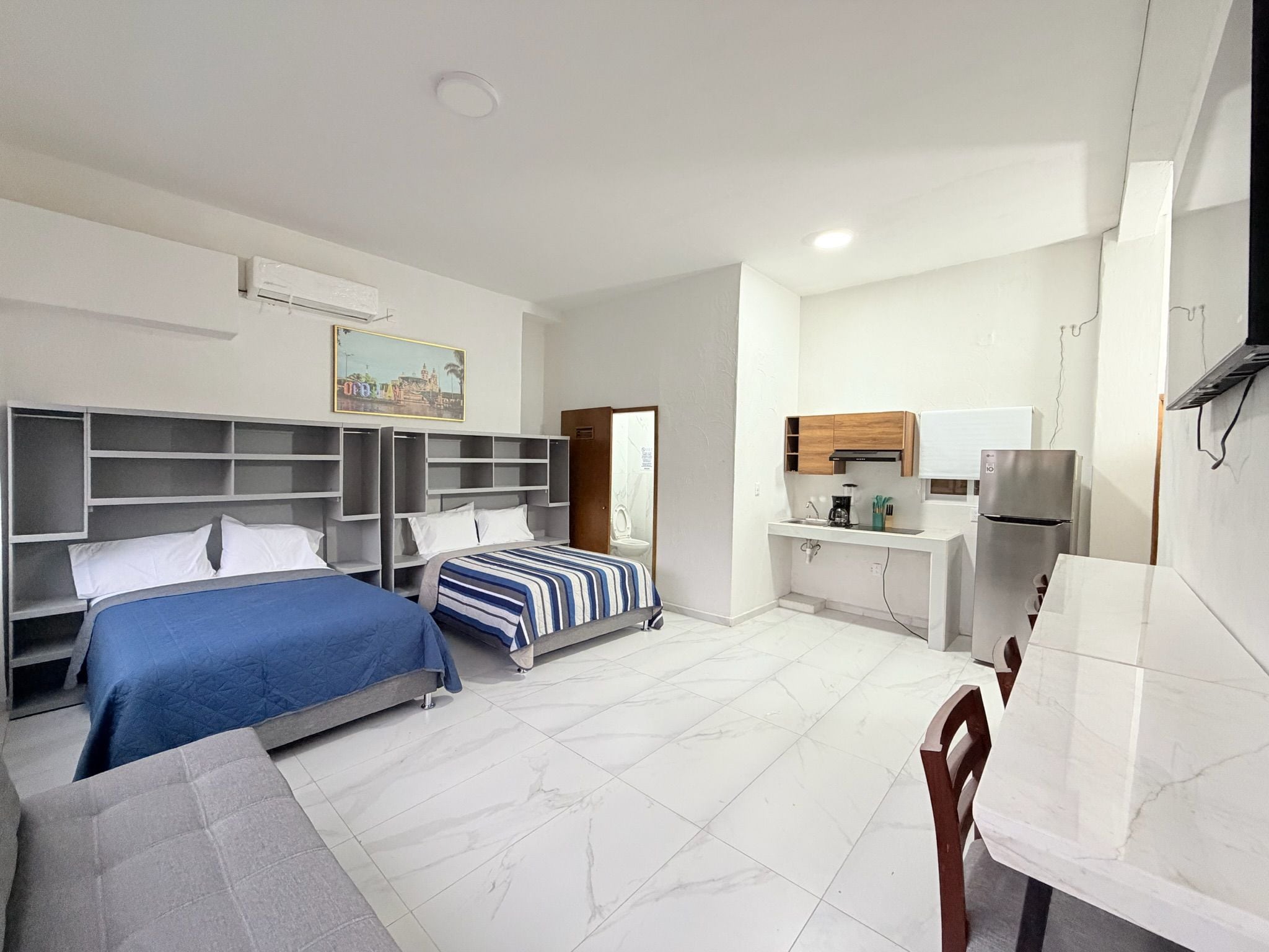 Una habitación de hotel con cama, escritorio, silla, kitchenette pequeña y baño.