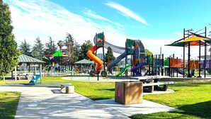 Ein Spielplatz mit verschiedenen Spielgeräten, einem Picknickbereich und einer Bank.