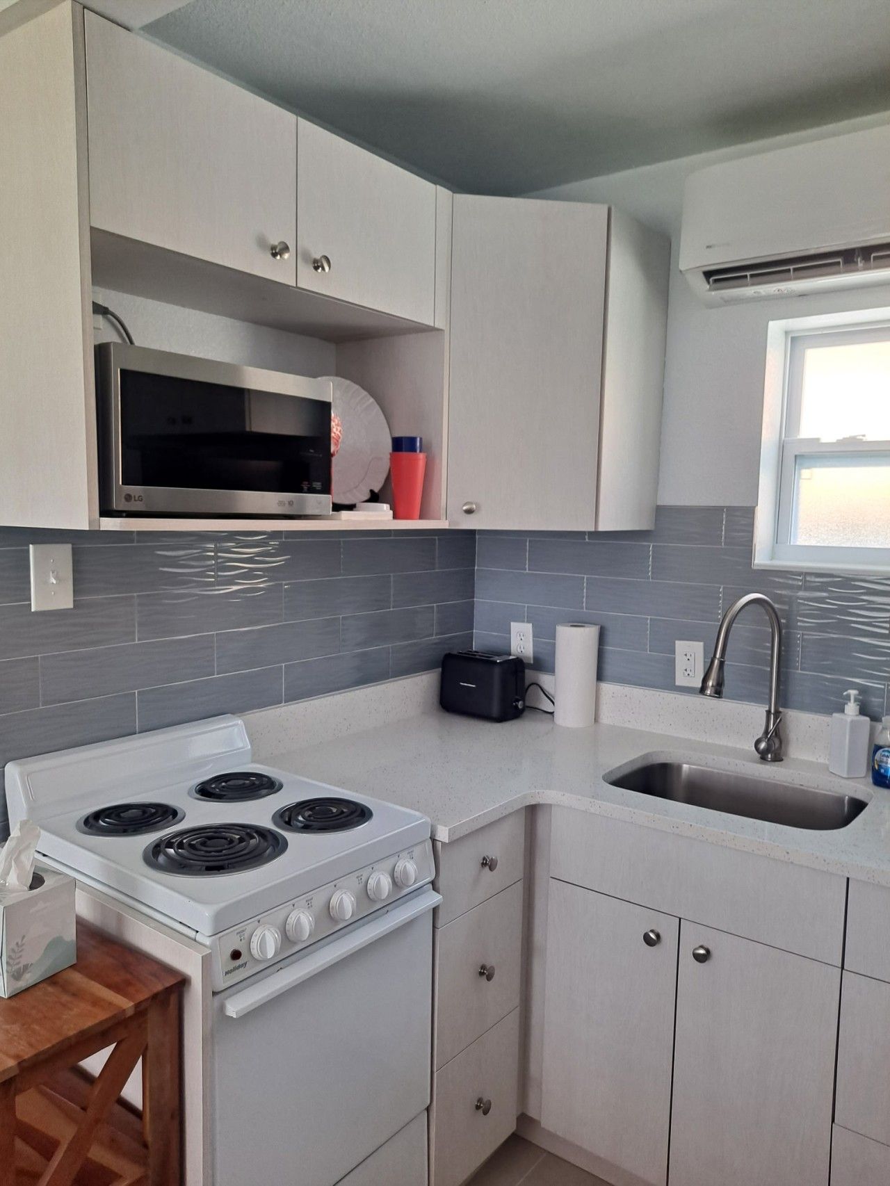 A compact kitchen with white cabinetry, a built-in microwave, a gas stove, a toaster, and a window providing natural light.