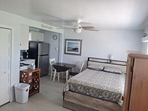 A compact room with a bed, a desk, a chair, a trash bin, a ceiling fan, and a refrigerator. - Beachside Mini-Condo on Redington Beach and Pool! (Redington Shores)
