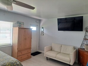 A room with a wooden wardrobe, a beige sofa, a flat-screen TV mounted on the wall, and a ceiling fan. - Beachside Mini-Condo on Redington Beach and Pool! (Redington Shores)