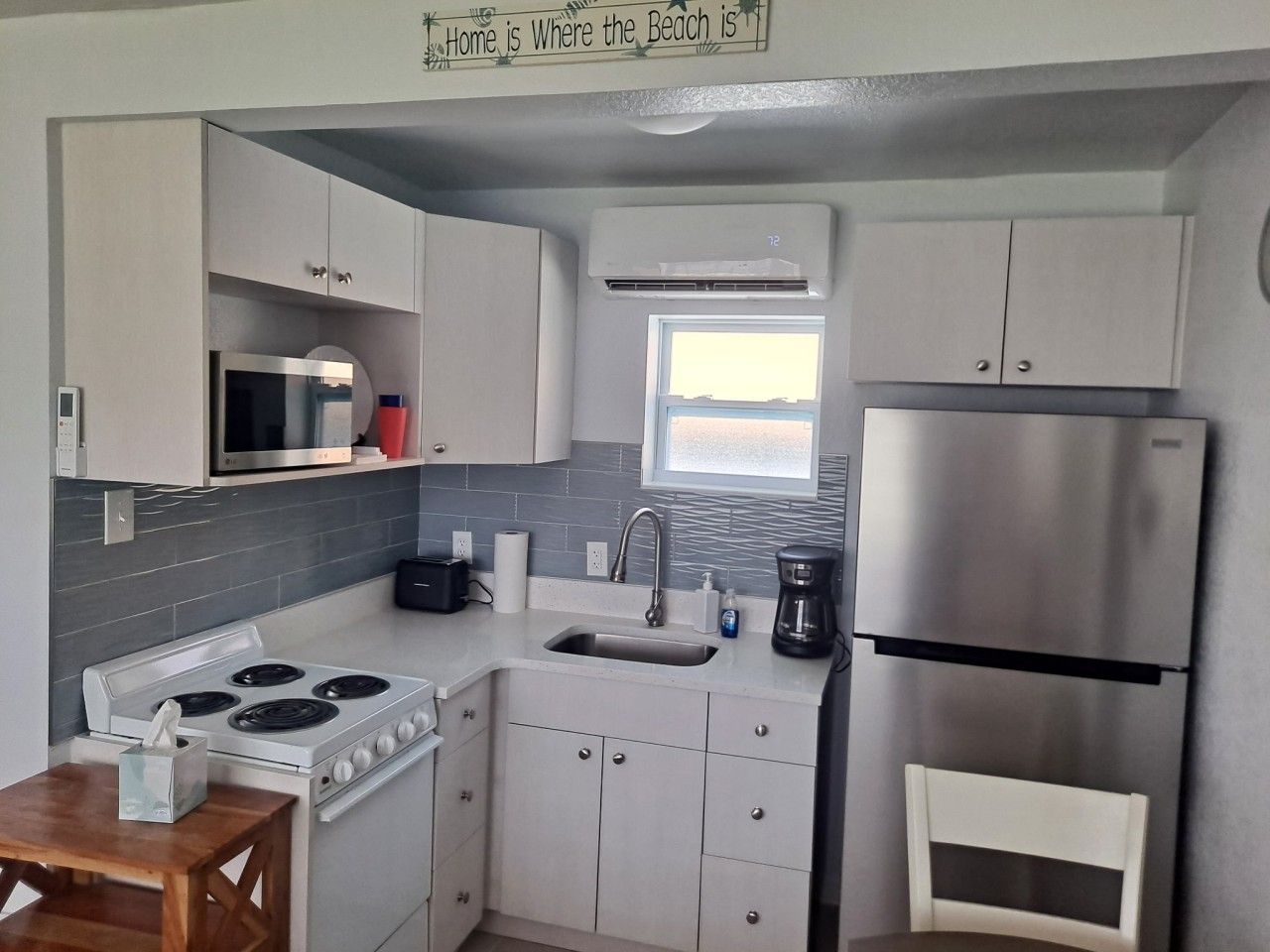 A compact kitchen with a gas stove, microwave, sink, and stainless steel refrigerator.