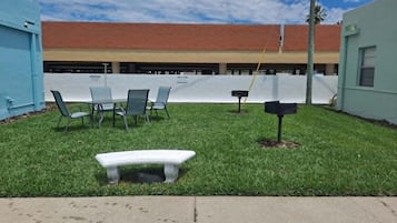 A grassy outdoor area with a bench, chairs, and a mailbox.