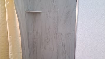 Un espace douche avec un mur en marbre et une porte blanche.