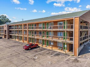 Un motel à plusieurs étages, doté d’un parking et d’une voiture rouge garée devant.