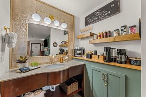 Une salle de bain dotée d’un grand miroir, d’un lavabo et d’un coin café avec divers appareils pour préparer le café.