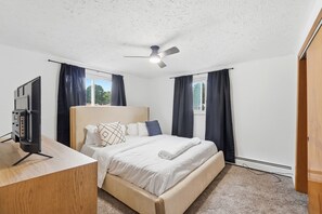 A hotel room with a bed, a desk, a ceiling fan, and a window with curtains. - Colerain King Suite - 30+ Day Stay (Groesbeck)
